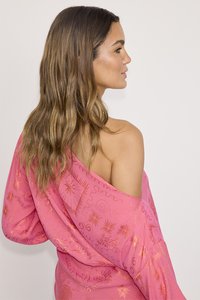 Haut rose à épaules dénudées avec des motifs dorés intricats, présentant une coupe décontractée et une texture de tissu douce. Le design comprend des accents brodés.