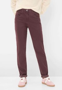 Pantaloni in twill di cotone color bordeaux con vita aderente, cinque tasche e orli arrotolati. Abbinati a sneakers rosa chiaro. Texture liscia.