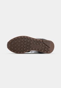 Semelle en caoutchouc marron avec des picots ronds et le logo "Saucony" au centre, vue du dessous sur fond blanc.