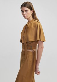 Bruine, kortelange blouse met een gestrikt knoopdetail en wijde mouwen, gecombineerd met een bijpassende hooggeknoopte rok met een strakke design.