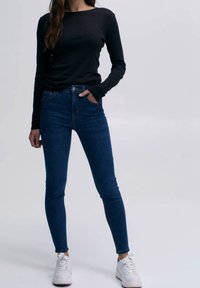 Camisa negra de manga larga combinada con jeans ajustados azules, con cintura alta y terminados con zapatillas blancas. Diseño simple y ceñido.