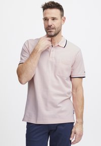 Világos rózsaszín pólóing, gallérral, két gombbal és mellzsebbel. A galléron és az ujjakon sötétkék díszcsíkok találhatók.