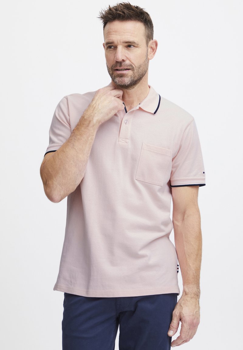 Világos rózsaszín pólóing, gallérral, két gombbal és mellzsebbel. A galléron és az ujjakon sötétkék díszcsíkok találhatók.