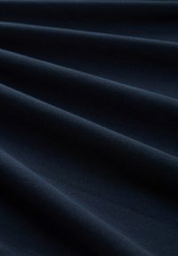 Dunkelblauer Stoff mit einer glatten Textur, der Falten aufweist, die einen leichten Glanz und ein gleichmäßiges Oberflächenmuster zeigen.