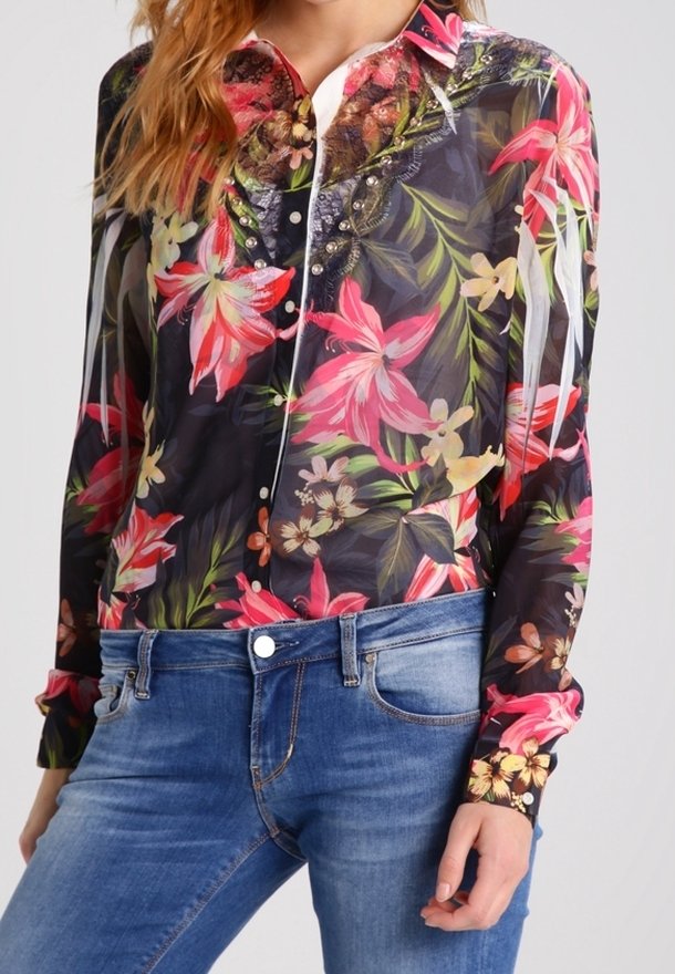 Femme portant un chemisier noir transparent à imprimé floral coloré rose et rouge et un jean en denim bleu, présenté de la poitrine jusqu'aux hanches.