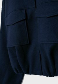 Tmavě námořnická bunda s dvěma předními klopovými kapsami a elastickým detailem na spodním lemu.