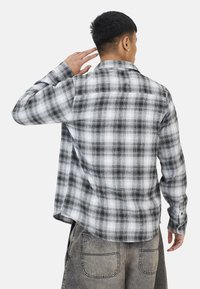 Grijze en witte geruite flanellen shirt met lange mouwen, een rugpas, en een zachte textuur, met een gebogen zoom en knoopmanchetten.
