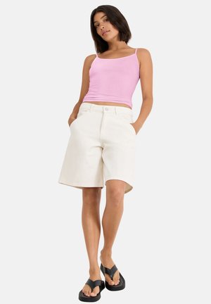 Shorts en denim blanc avec poches latérales, coupe décontractée et ourlet effiloché, assortis à un débardeur rose ajusté et des tongs noires.