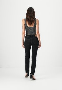 Black denim jeans with a slim fit and minimalistic design. Features back pockets and a small brand patch. Textured black and silver top.