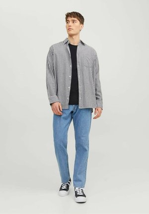 Oversized black and white checkered shirt, buttoned, worn over a black t-shirt, paired with light blue jeans and black sneakers.