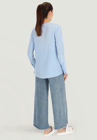 Jasnoniebieska bluzka z długim rękawem o okrągłym dekolcie, zestawiona z szerokimi spodniami z jasnego dżinsu i białymi klapkami. Standardowy krój, gładka tekstura.