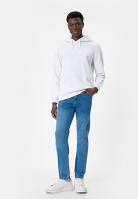 Sudadera blanca con cordones, combinada con jeans azul claro y zapatillas blancas. La sudadera tiene una textura suave y un corte relajado.