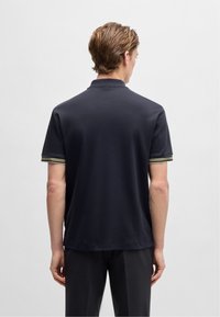 Granatowa koszulka polo z krótkim rękawem, z prążkowanymi akcentami w kolorze zielonym i białym na mankietach. Gładki materiał i klasyczny krój kołnierzyka.