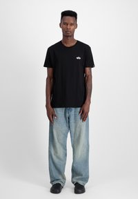 Sort bomulds t-shirt med rund hals og korte ærmer, med et lille broderet design på brystet. Båret med lyseblå løse jeans.