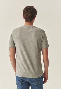 Szürke pamut rövid ujjú póló, kerek nyakkivágással és sima textúrával, kék farmernadrággal párosítva. Egyszerű dizájn, látható minták nélkül.