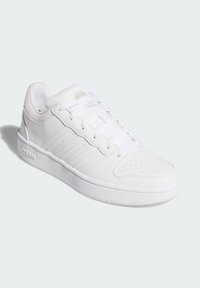 Biele športové topánky s hladkým koženým zvrškom, perforovanou špičkou a tromi embosovanými pruhmi po stranách. Obsahujú ploché šnúrky a gumové podrážky.