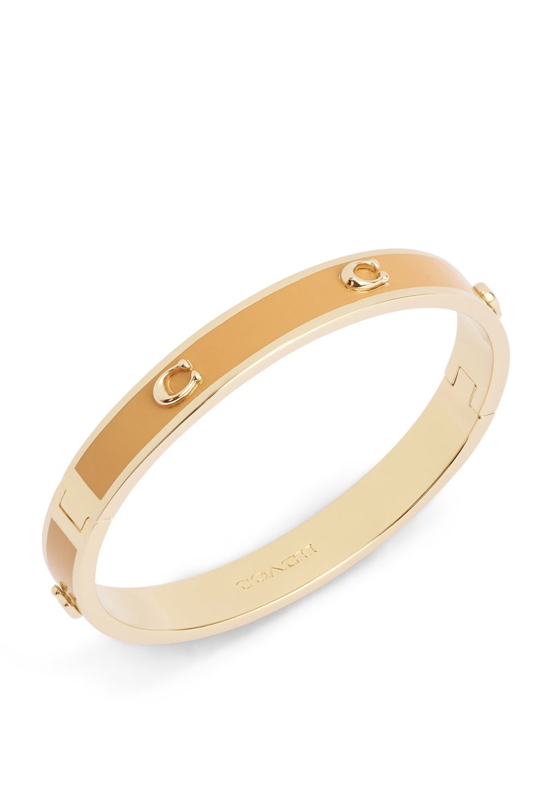 Bracciale rigido dorato con inserto in smalto beige liscio e dettagli hardware in rilievo. Presenta un design elegante e arrotondato.