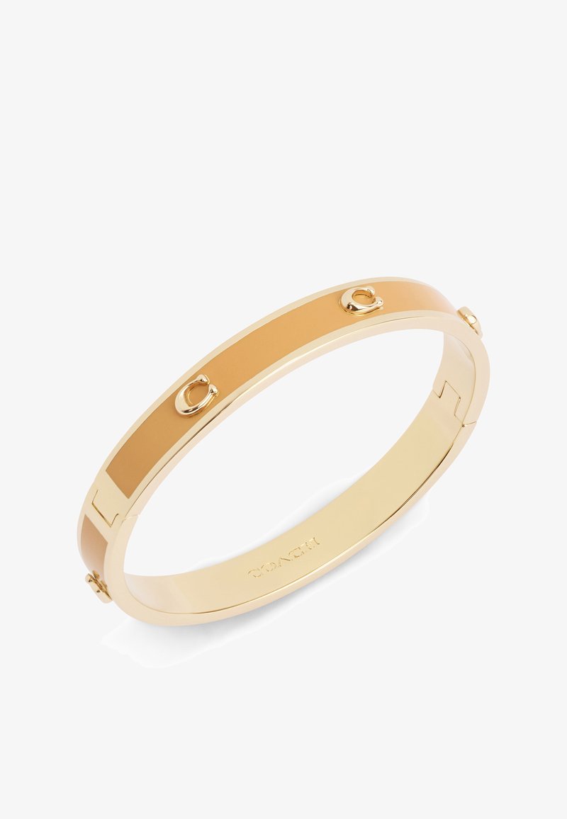 Bracciale rigido dorato con inserto in smalto beige liscio e dettagli hardware in rilievo. Presenta un design elegante e arrotondato.