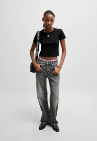 T-shirt preto cropped com logotipo branco, jeans cinza de perna larga com leve desbotado e botas ankle pretas; bolsa preta com alça de logotipo.