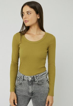 Haut à manches longues, de couleur vert olive, avec un col arrondi, accompagné d'un jean taille haute délavé gris clair avec une fermeture à boutons.