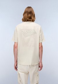 Beige bomulds t-shirt med et stort grafisk print i en lysere nuance på ryggen, med tekst og abstrakte designelementer, afslappet pasform.