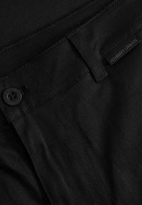 Černá bavlněná tkanina s knoflíkovým zapínáním, zesíleným šitím a štítkem s nápisem "JOHNNY URBAN." Hladký povrch s matným finišem.