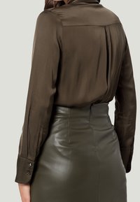 Blouse en soie marron avec un empiècement au dos et des manches longues, assortie à une jupe en cuir verte taille haute avec un design ajusté et des accents de boutons.