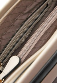 Interno di una borsa beige con zip scura a contrasto, foderato in morbido tessuto taupe con sottili motivi; include più scomparti per l'organizzazione.