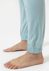 Lichtblauwe katoenen broek met gathered cuffs, met een zachte textuur. Blote voeten zichtbaar, met de nadruk op het enkelgebied.