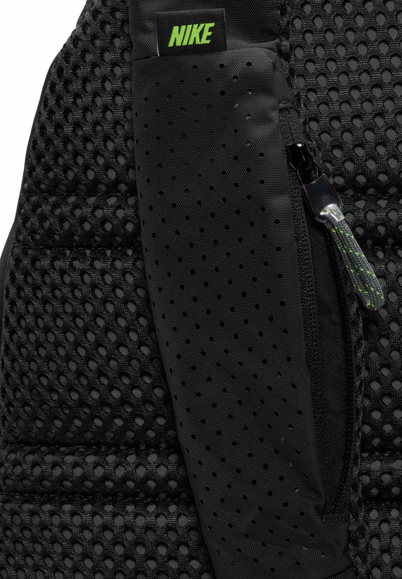 Czarny plecak z teksturowanej tkaniny siateczkowej, gładką czarną kieszenią na zamek błyskawiczny oraz zielonym logo Nike na pasku.