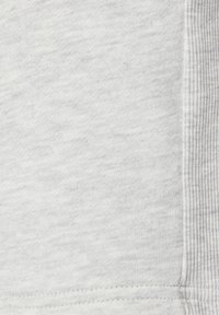 Tissu gris clair présentant une surface douce et texturée avec un accent à rayures horizontales le long du bord droit. Détails de couture visibles.