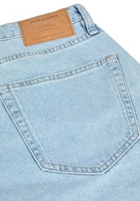 Jeans de mezclilla azul claro con un bolsillo trasero. Superficie texturizada con costuras visibles. Etiqueta de cuero en la cintura que dice "JACK & JONES."