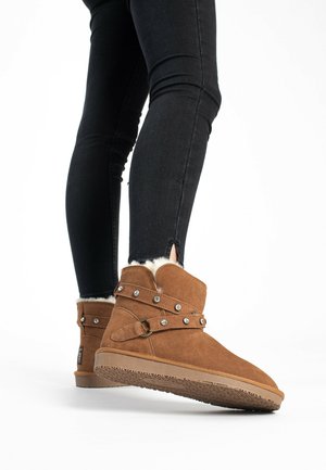 Tan Suede-Ankleboots mit Kunstfellfutter, Schnalle und Nietenakzenten sowie einer strukturierten Gummisohle. Kombiniert mit schwarzen Skinny Jeans.