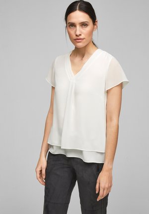Blusa bianca, leggera, a maniche corte con scollatura a V e silhouette stratificata, caratterizzata da morbide pieghe nella zona del collo. Tessuto liscio.