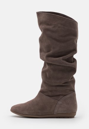 Botte plate haute jusqu'au genou en daim marron avec tige souple et bout arrondi sur fond clair.