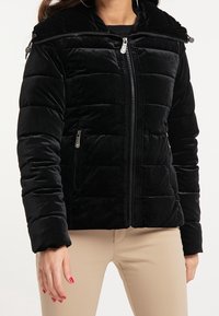 Svart sammet puffjacka med en zip-up huva, horisontellt quiltat mönster och sidofickor. Har en frontdragkedja och en avslappnad passform.
