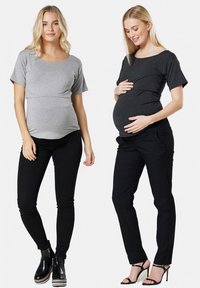 Două modele poartă bluze de maternitate: una gri cu mâneci scurte și una neagră cu mâneci scurte, ambele fiind asortate cu pantaloni negri.