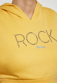 Felpa gialla con la scritta "ROCK" in borchie metalliche e "my soul" ricamato in blu. Tessuto morbido, design casual con tasca frontale.