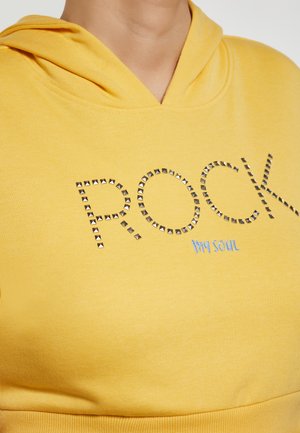 Sárga kapucnis pulóver, amelyen a "ROCK" fémes tüskékből készült, kék hímzett "my soul" felirattal. Puha anyagú, laza fazonú, elülső zsebes.