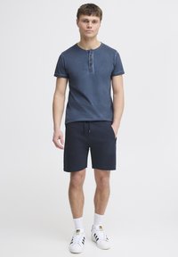 Marineblauwe henley t-shirt met drie knopen, gecombineerd met marineblauwe shorts en witte sneakers met zwarte strepen. Katoenmengsel, casual ontwerp.