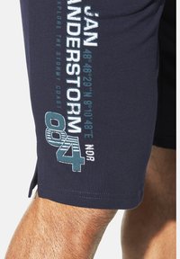 Dunkelblaue Shorts aus weichem Stoff, mit weißen und türkisfarbenen Texten und Grafiken an der Seite, sowie seitlichen Schlitzen für angenehmen Tragekomfort.