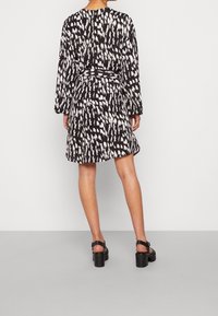 Svartvit mönstrad klänning med långa ärmar, midjebälte och utsvängd kjol. Slät tyg med grafisk design över hela.