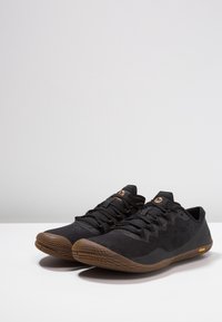 Czarne buty sportowe z teksturowaną siateczką, gumową podeszwą oraz pomarańczowym logo na języku. Niskoprofilowy design z elastycznym dopasowaniem.