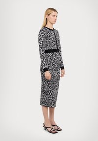 Robe à imprimé léopard en noir et blanc, design ajusté avec une taille noire accentuée et des manches longues. Associée à des sandales noires à lanières.