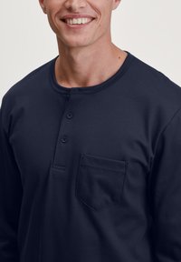 Donkerblauwe lange mouwen henley shirt met een ronde halslijn, twee knopen bij de kraag en een borstzak. Soepele stofstructuur.