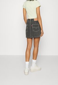 Sort denim mini-nederdel med hvid syning, baglommer og et synligt mærke på taljebåndet. Sammen med en lys grøn top og hvide sko.