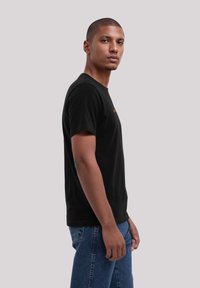 Black cotton t-shirt with short sleeves and a crew neckline. Features subtle orange text on the chest. Model standing in profile.