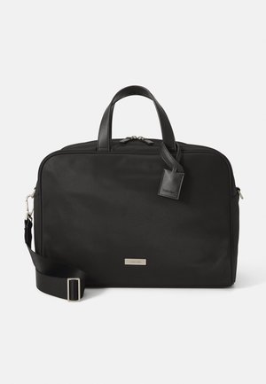 Sac à dos en nylon noir avec des accents en cuir, deux anses supérieures, une bandoulière ajustable et une étiquette de marque sur le devant.