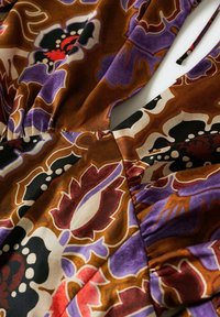 Gros plan d'un tissu avec des motifs floraux vifs en marron, violet, noir, rouge et blanc et un détail de couture froncée.