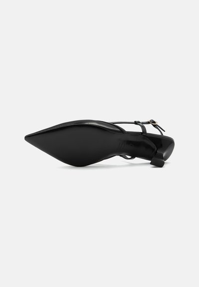 Chaussure slingback noire à bout pointu avec un petit talon kitten et une bride à la cheville avec une boucle dorée, vue du côté de la semelle.